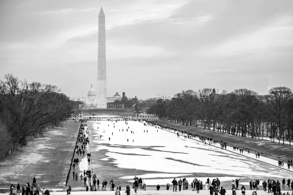 National Mall in winter with snow and people walking around, Washington Monument obelisk visible in background.